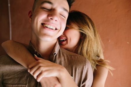 girl hugging guy from behind on a background of an orange wall