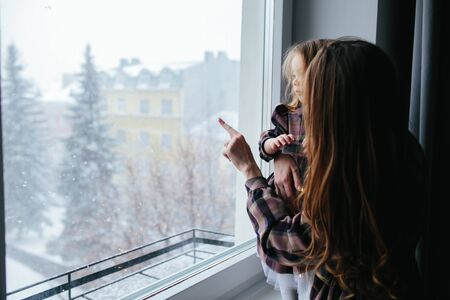 Mom with little girl looking through the windowの写真素材