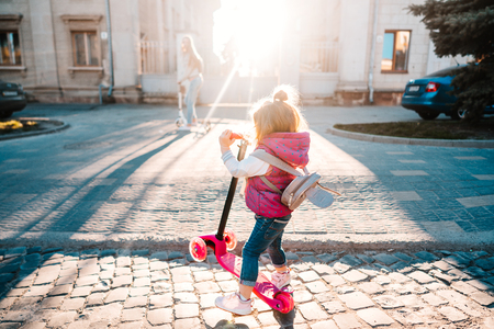 Little girl with blonde hair rides on scooterの写真素材