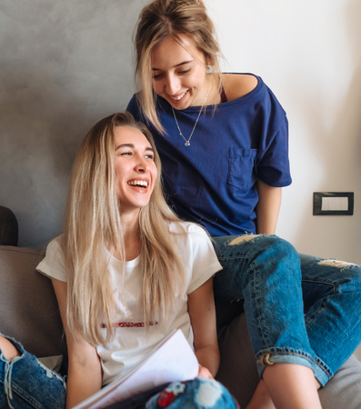 Two young girls on a couch watching magazineの写真素材