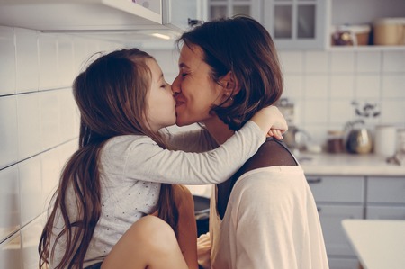 Mom kisses her little daughter in the kitchenの写真素材