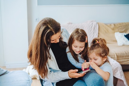 Mom and two daughters are looking at the smartphoneの写真素材