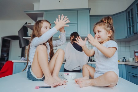 Two little girls in the kitchen sitting on the table.の写真素材