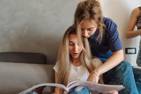 Two young girls on a couch watching magazineの写真素材
