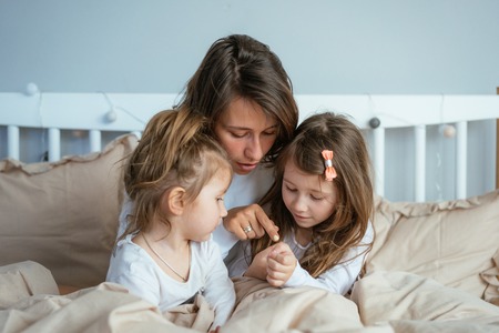 Mom and two daughters draw in bedの写真素材