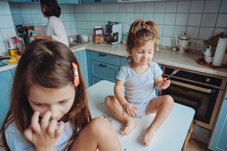 Two little girls in the kitchen sitting on the table.の写真素材