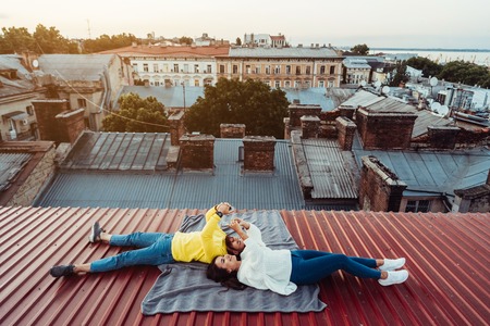 A handsome guy and a young girl lie on the roof and hold the smarfons.