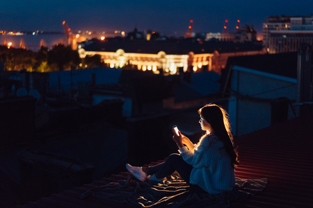 Young girl sits at night on the roof of a house. Beautiful eveningの写真素材