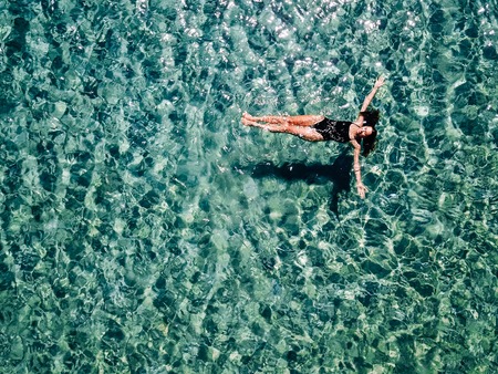 Young girl in a black swimsuit swims in the sea.