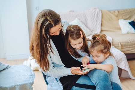 Mom and two daughters are looking at the smartphoneの写真素材
