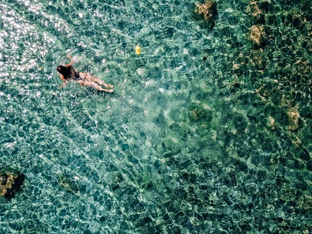 Young, beautiful girl in a black swimsuit swims in the sea.の写真素材