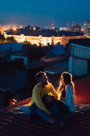 Loving couple is sitting on the roof of the house. Beautiful eveningの写真素材