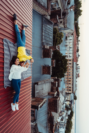 A handsome guy and a young girl lie on the roof and hold the smarfons.の写真素材