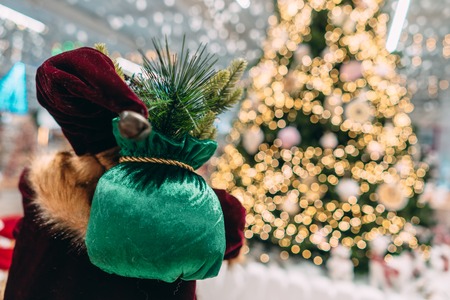 Santa from behind with gift bag on background of bokeh christmas tree.の写真素材