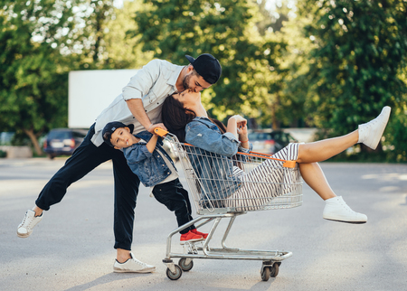 Young dad carries mom and son in a cart on the parking lotの写真素材