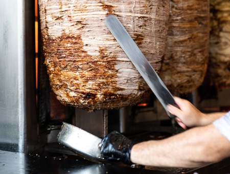 Mans hands holding a knife, cutting slices from a vertical skewerの写真素材