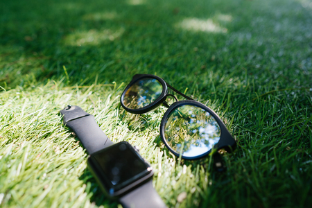 Smart watch and sunglasses lie on the grassの写真素材
