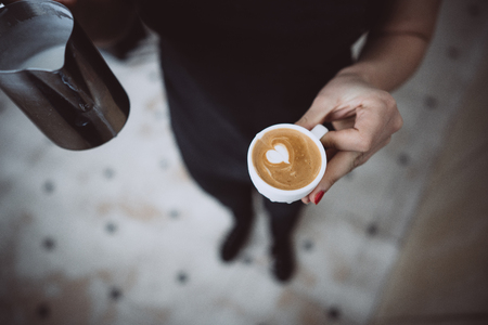 Barista holds two cups, with milk and latteの写真素材