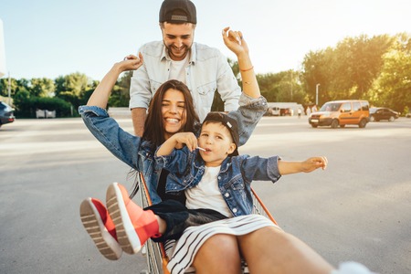 Young dad carries mom and son in a cart on the parking lotの写真素材