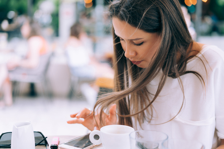 Attractive woman is sitting in a summer street cafe with a phone.の写真素材