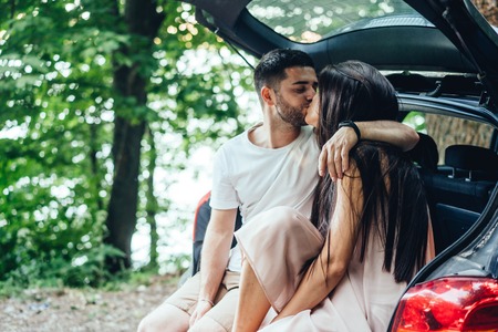 Young, happy couple is sitting in the trunk of their car.の写真素材