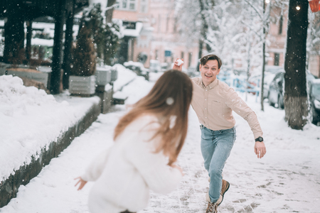 Joyful young couple in sweaters is playing snowballs at the street.の写真素材