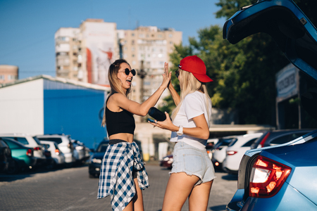Two young girls in sunglasses posing for the camera on the car parking.の写真素材