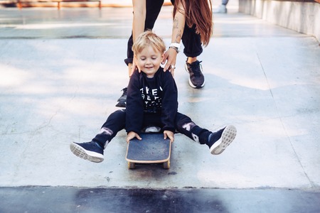 Young mother teaches her little boy to ride a skateboardの写真素材