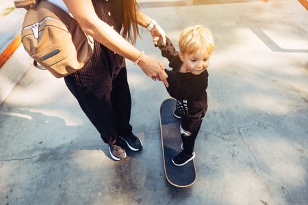 Young mother teaches her little boy to ride a skateboardの写真素材