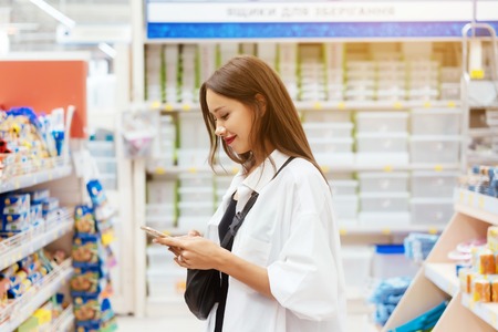Smiling young woman with smartphone in supermarketの写真素材