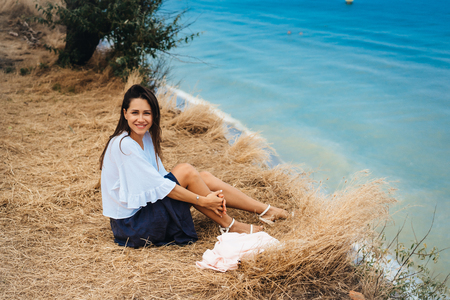 attractive woman in summer skirt and shirt sits on the shoreの写真素材