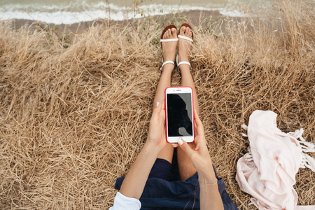 beautiful young girl sitting and holding a smartphone in her hands, top viewの写真素材