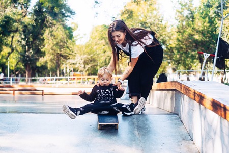 Young mother teaches her little boy to ride a skateboard