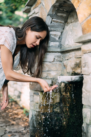 Beautiful, young girl drinks spring water outdoorの写真素材