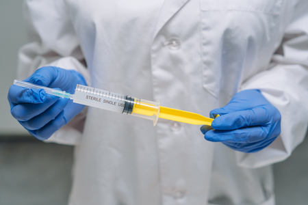Hands in rubber gloves hold a disposable medical syringe with the drug, close angleの写真素材