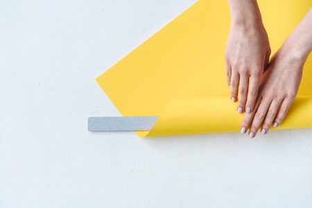 Womens hands wrap a gray nail file in paper