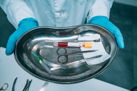 Nurse in rubber gloves holding a tray of surgical medical equipment, close viewの写真素材