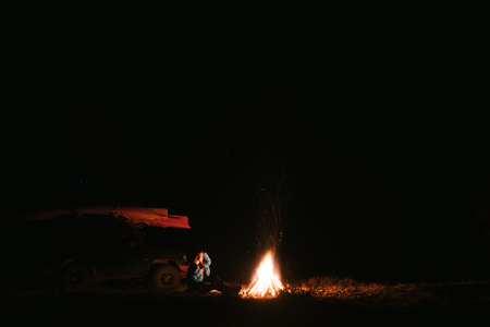 Woman sitting and getting warm near the bonfire in the night forest.の写真素材