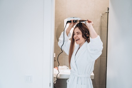 Beautiful smiling woman curling long hair using curling iron.の写真素材