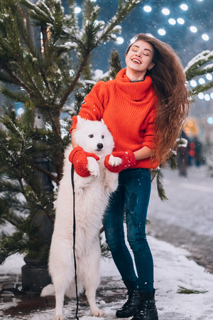 A woman is hugging her dog on a night street.の写真素材