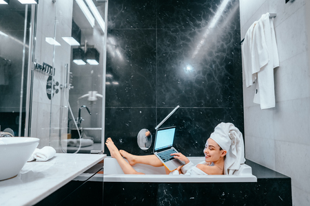 Relaxed woman with towel on hair lying in bathtubの写真素材