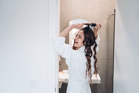 Beautiful smiling woman curling long hair using curling iron.の写真素材