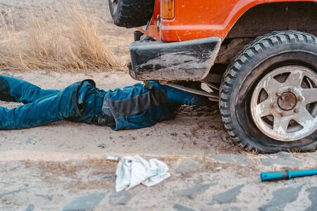 man lies under a 4x4 car on a dirt roadの写真素材