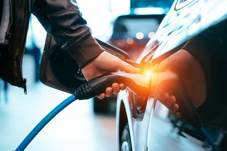 Human hand is holding Electric Car Charging connect to Electric car