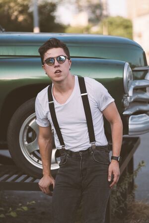 Guy in a shirt with suspenders posing at the retro car