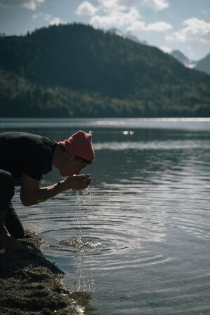 A man washes his hands on the shore of a forest lake in the mountains