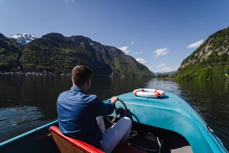 Handsome young guy controls a motorboat on a mountain lake, the mountains in the backgroundの写真素材