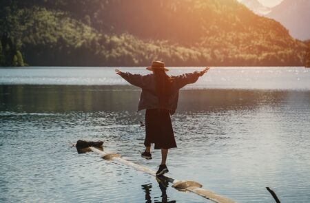 The girl in the dress and hat of the lake in the mountains to hold balanceの写真素材