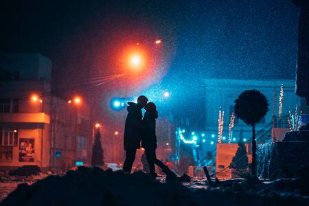 Young adult couple in each other's arms on snow covered street. Peaceful atmosphere in snowy winter...
