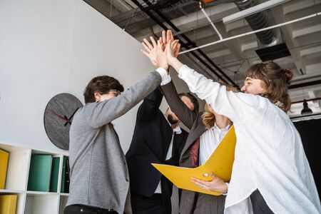 Cheerful young group of people standing in the office and giving high five